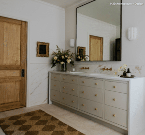 Modern bathroom vanity with light gray cabinetry, brass knobs, marble backsplash, and a large framed mirror above two sinks.