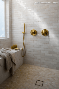 Modern bathroom with white subway tiles, gold shower fixtures, and a freestanding tub; sunlight on the wall.
