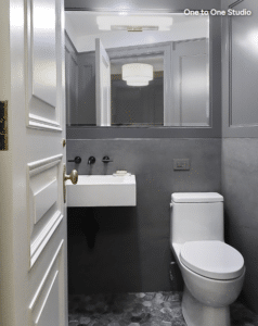 A modern bathroom with a wall-mounted sink, white toilet, and large mirror reflecting a ceiling light; door is open.