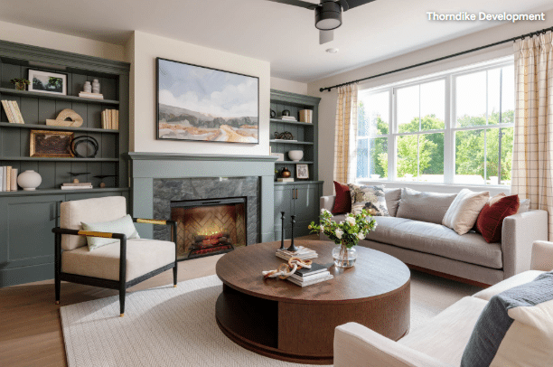 Intrepid Blog Living room with dark green built‑in shelves around a stone fireplace, a round wooden coffee table, and a gray sofa by a large window.