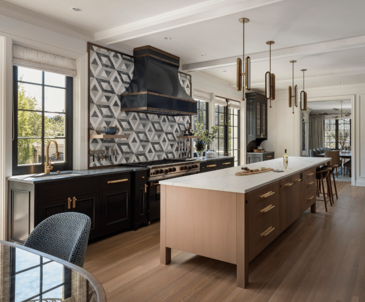 Intrepid Blog Modern kitchen with geometric tile backsplash, black range, brass hardware, and a large marble-topped island; natural light from windows fills the room.